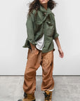 Tan satin Free City AirJump Pant 26 paired with a green sunfade jacket and boots on gray concrete.