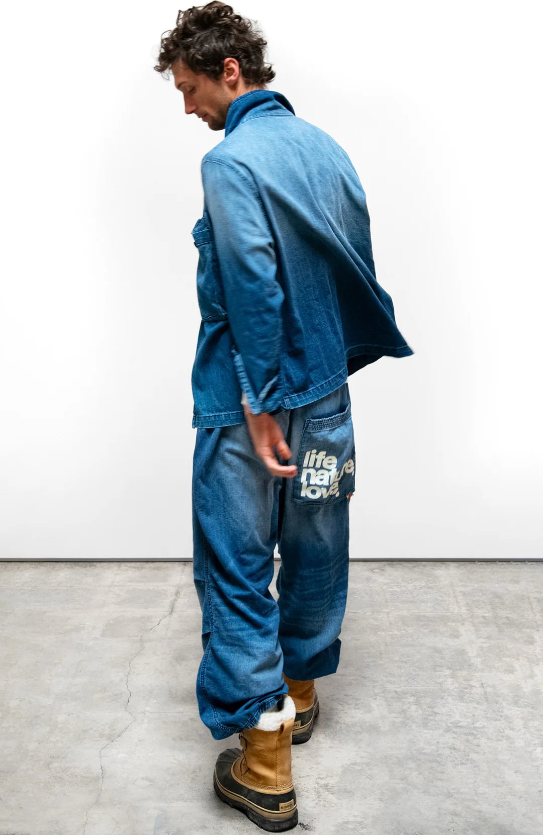 Free City Indigo Workshop Biggy Shirt with tan boots, lifahalove detail, shown on concrete floor at Bungalow Furniture.
