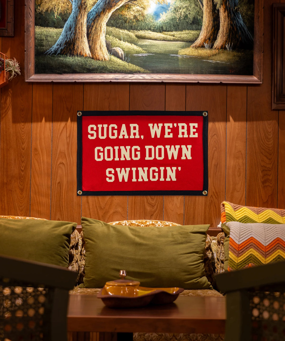 Couch with green pillows in a cozy room, A Faire camp flag above featuring playful text for a relaxed vibe.