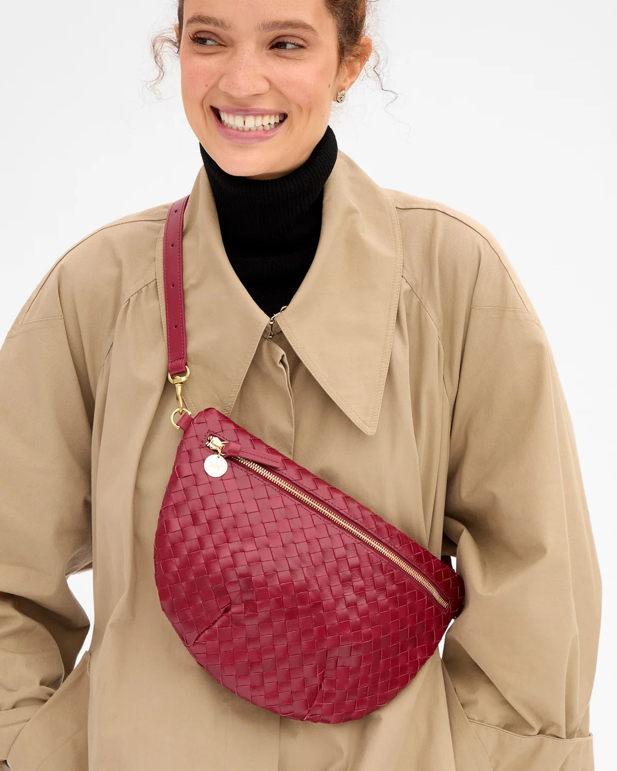 Clare Vivier Grande Fanny S26 handwoven leather crossbody with gold zipper, worn with a tan trench coat.