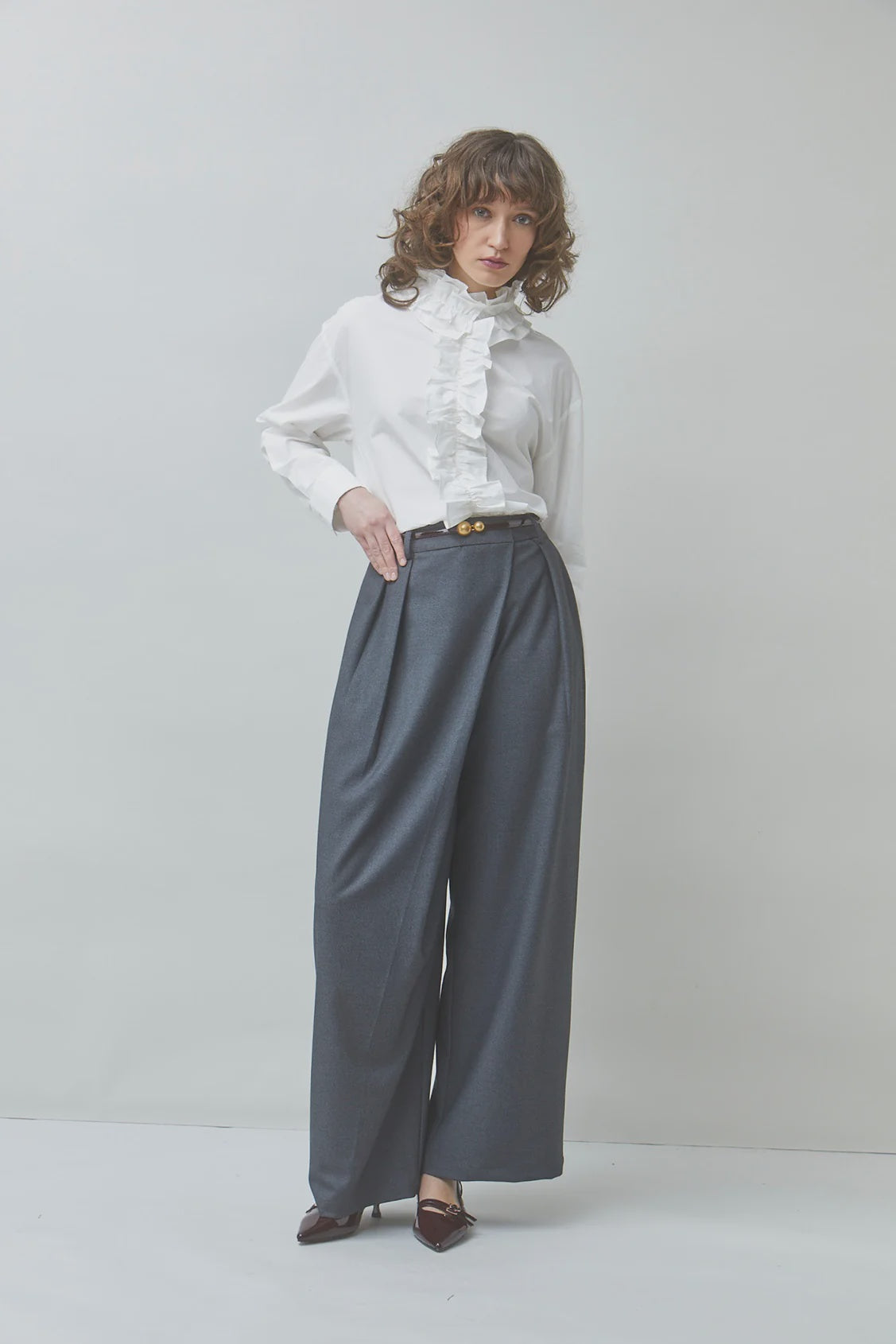 White ruffled blouse and high-waisted grey trousers by SUNCOO, styled against a light gray background.