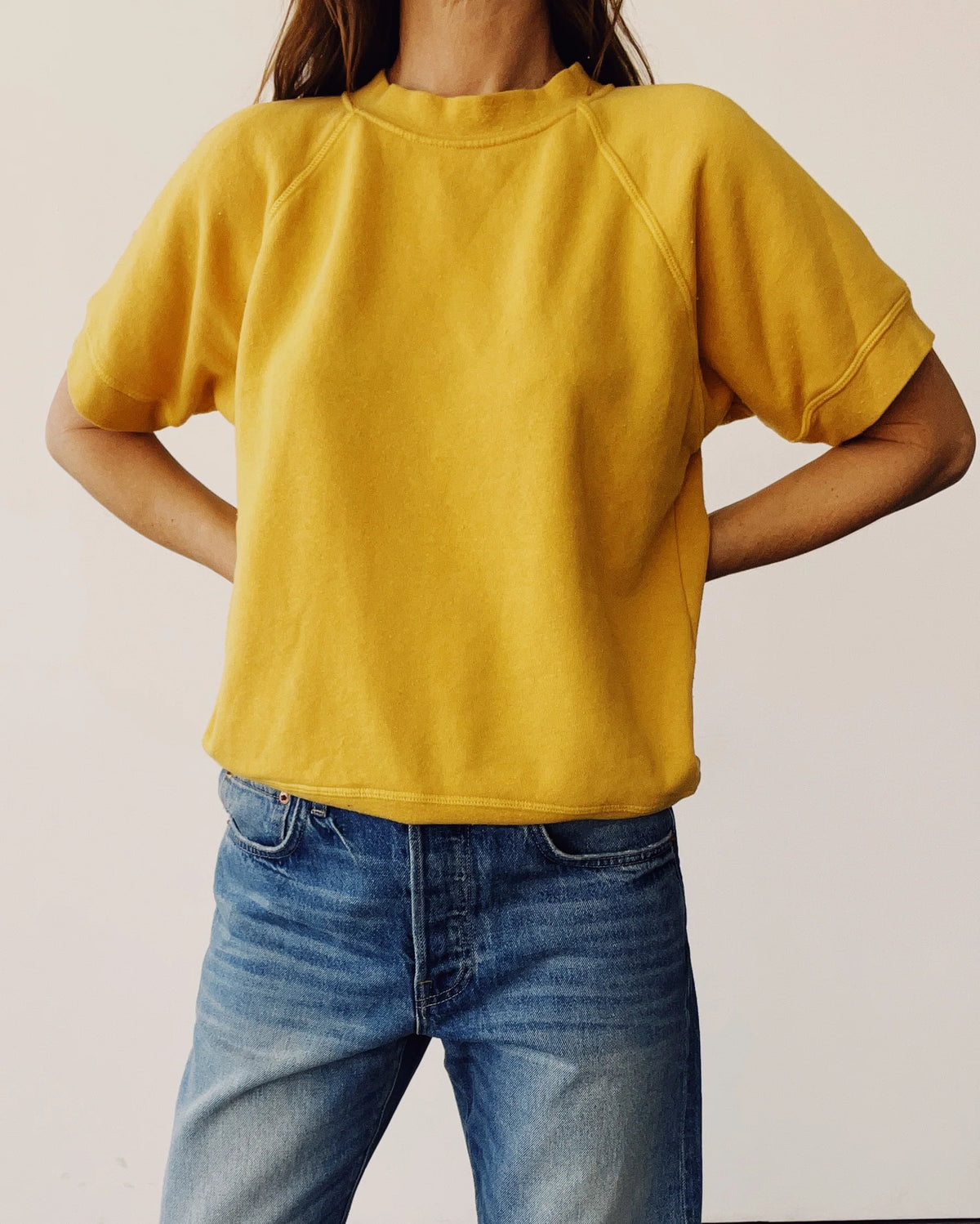 Hey Gang S/S Sweatshirt in goldenrod paired with blue jeans, shown on model hands on hips against plain background.