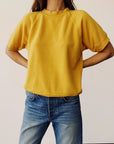 Hey Gang S/S Sweatshirt in goldenrod paired with blue jeans, shown on model hands on hips against plain background.