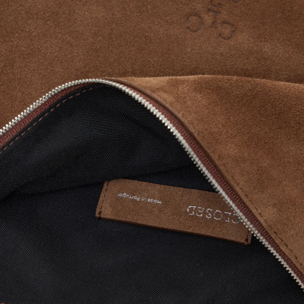 Brown suede halfmoon bag with silver zipper and adjustable strap by CLOSED, partial logo visible.