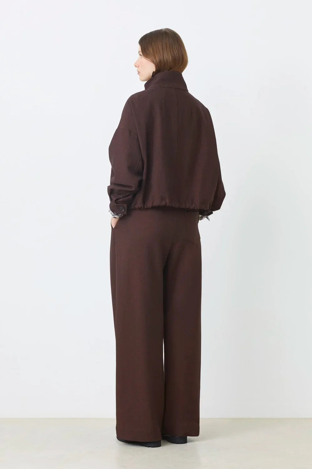 SUNCOO Dona chocolate brown jacket and wide-leg pants seen from the back, modeled by a woman with short brown hair.
