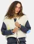 Kerri Rosenthal Coze Magoze Vest styled with a dark patched sweatshirt and pink glasses, worn by a woman with curly hair.