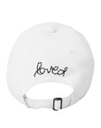 The Baseball Hat Heart Patch by Kerri Rosenthal is a white cap viewed from the back, with "loved" in black script and a small heart above the adjustable strap, reflecting popular styles.