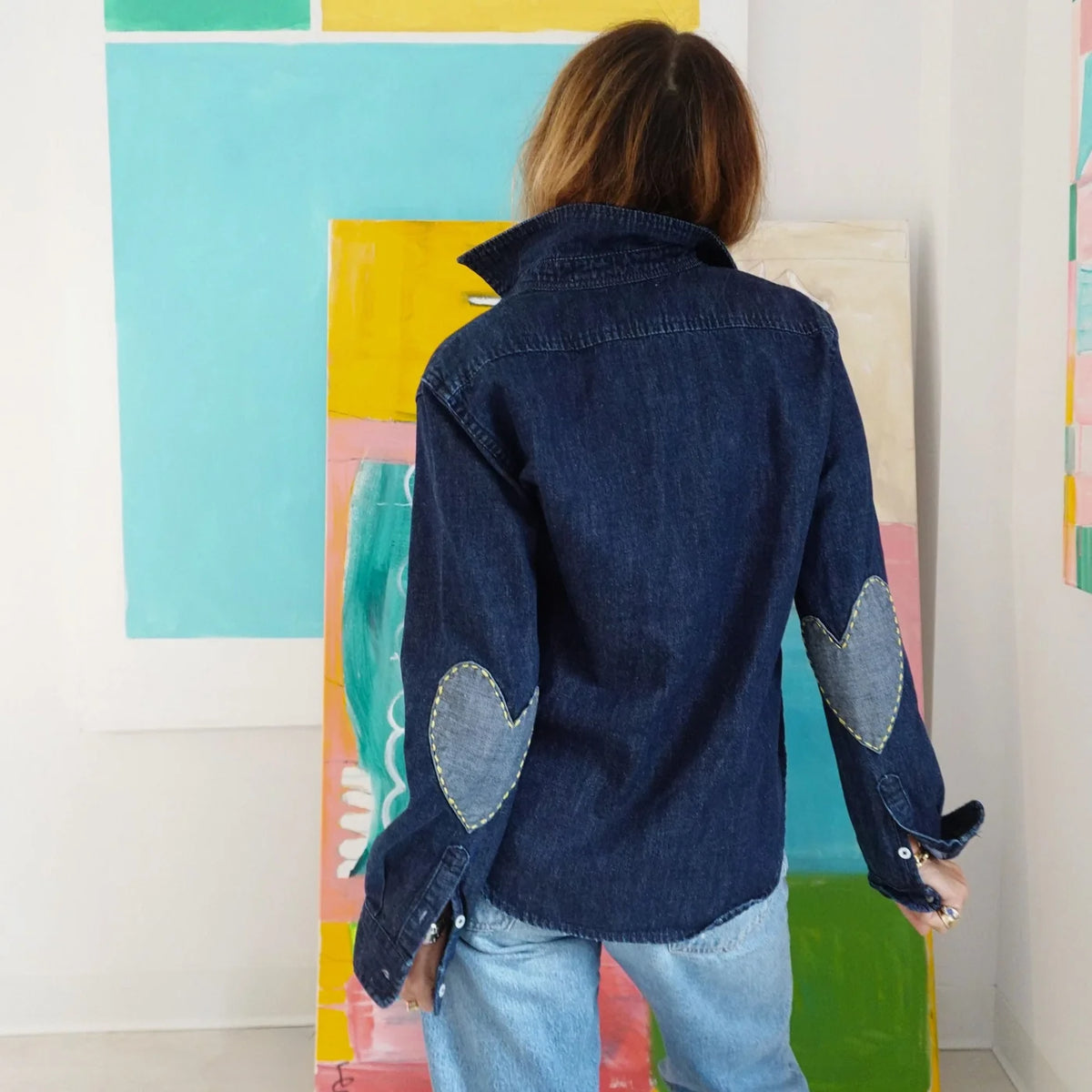 Keaton Denim Shirt by Kerri Rosenthal with heart elbow patches, shown from the back, abstract art setting.