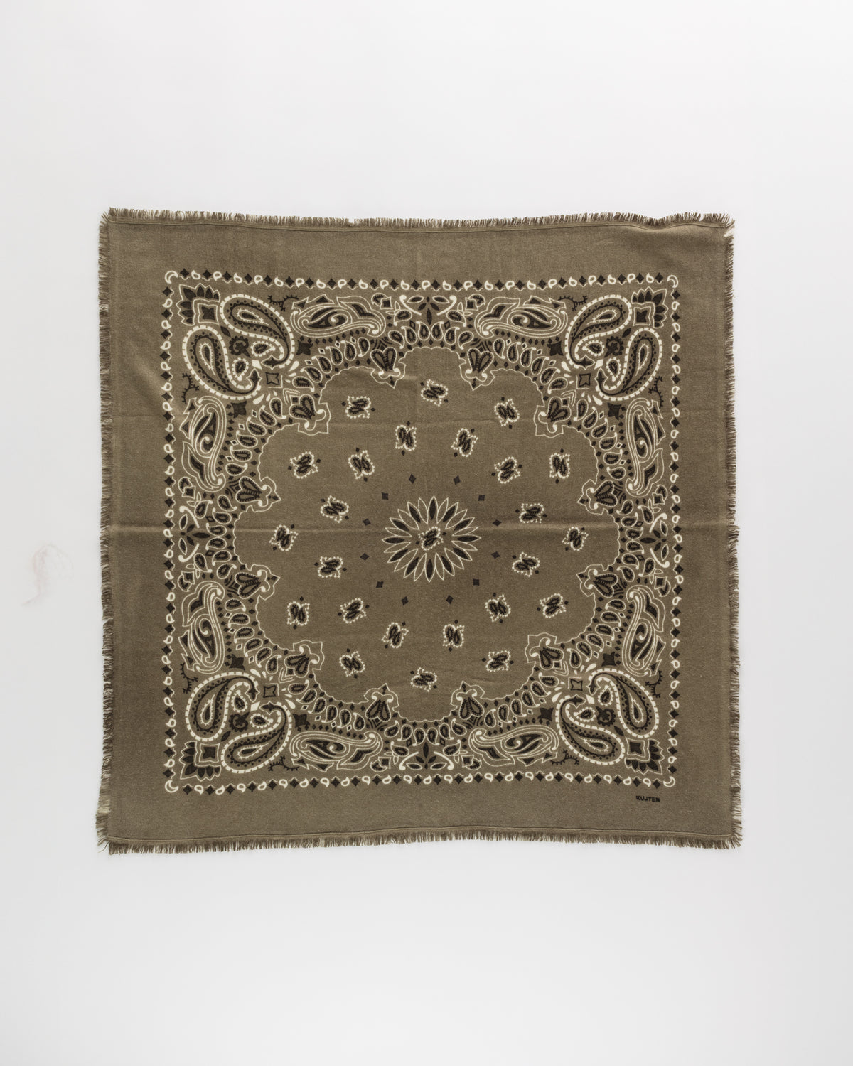 The Hachiko Scarf by KUJTEN is a square olive green bandana in printed cashmere, showcasing white and black paisley and floral designs, frayed edges, and a textured finish. It’s presented on a plain white background.