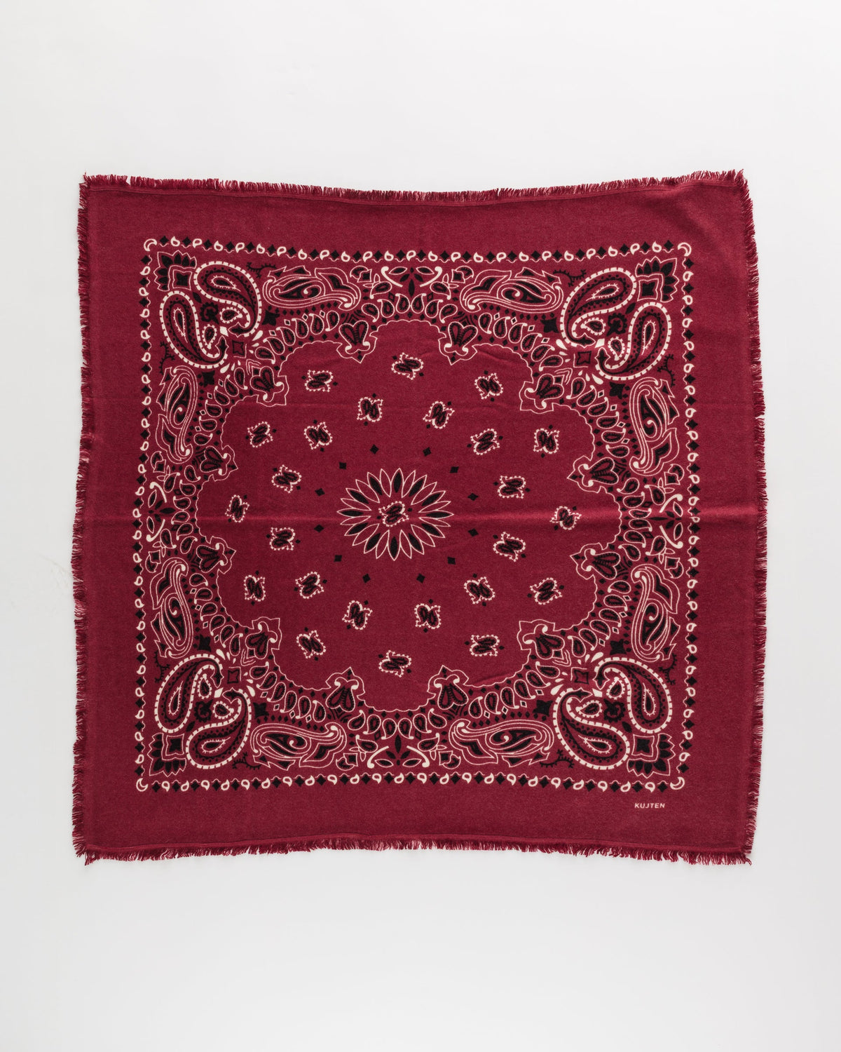 The Hachiko Scarf by KUJTEN features a red, white, and black paisley pattern with fringed edges and a central floral motif, crafted from soft printed cashmere jersey and shown flat on a white background.