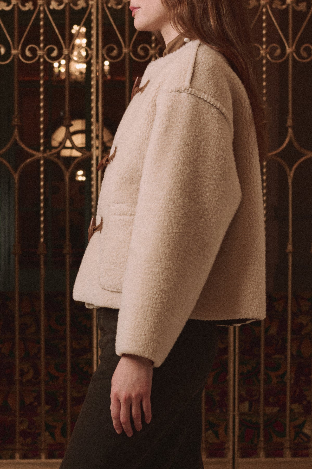 Woodside Toggle Coat by The Great Inc. in a classic style, shown indoors with ornate ironwork in the background.