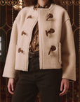 The Great Inc. Woodside Toggle Coat in brown, styled over dark pants and shirt, worn indoors for a modern look.