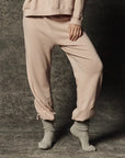 The Great Inc. Dance Pant in dark fabric, worn with gray socks, model stands on a textured gray floor.