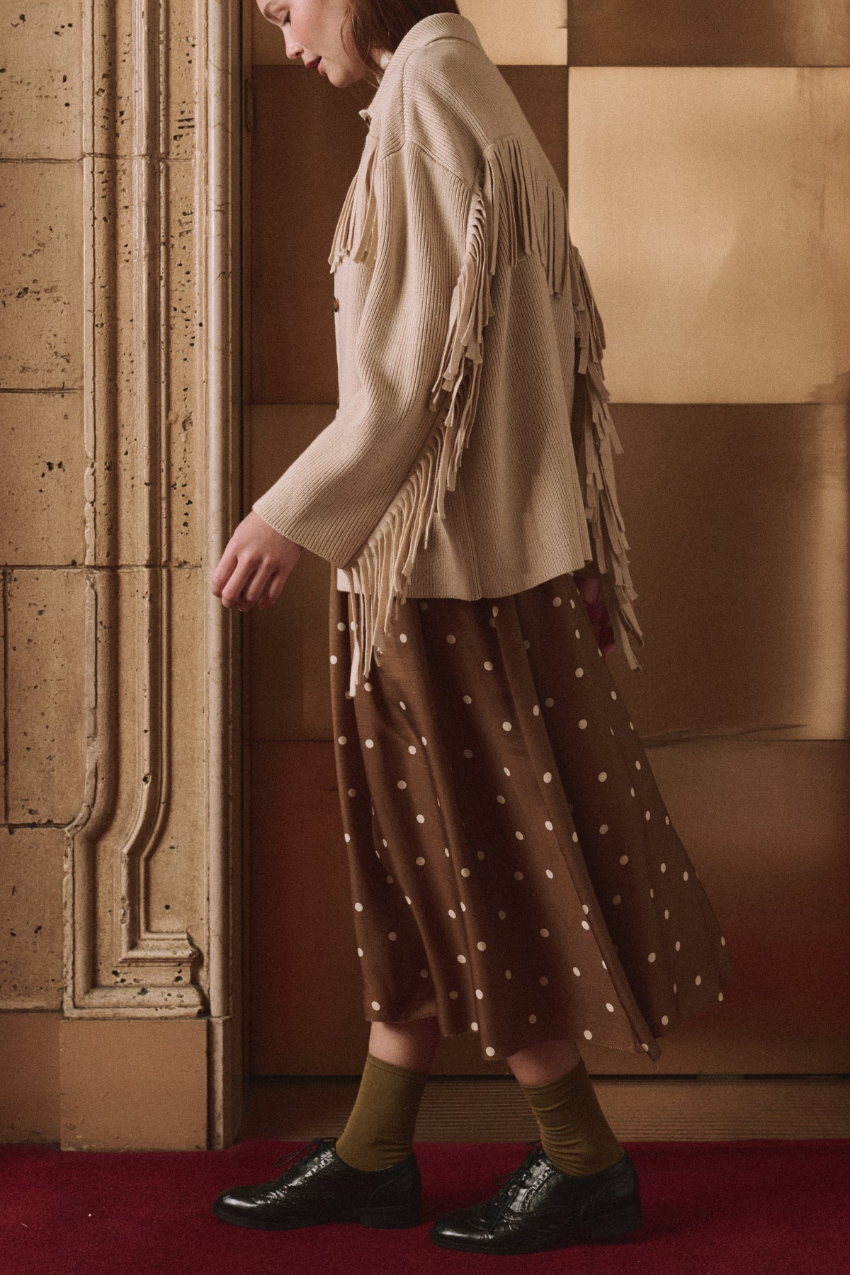 Western Fringe Sweater Jacket by The Great Inc. styled with a polka dot skirt on a red carpet backdrop.