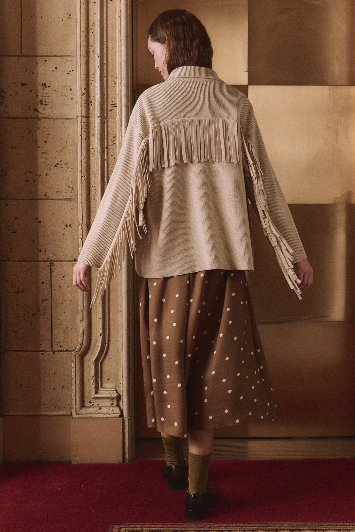 Western Fringe Sweater Jacket by The Great Inc., cream with fringe, styled with a brown polka dot skirt on red carpet.