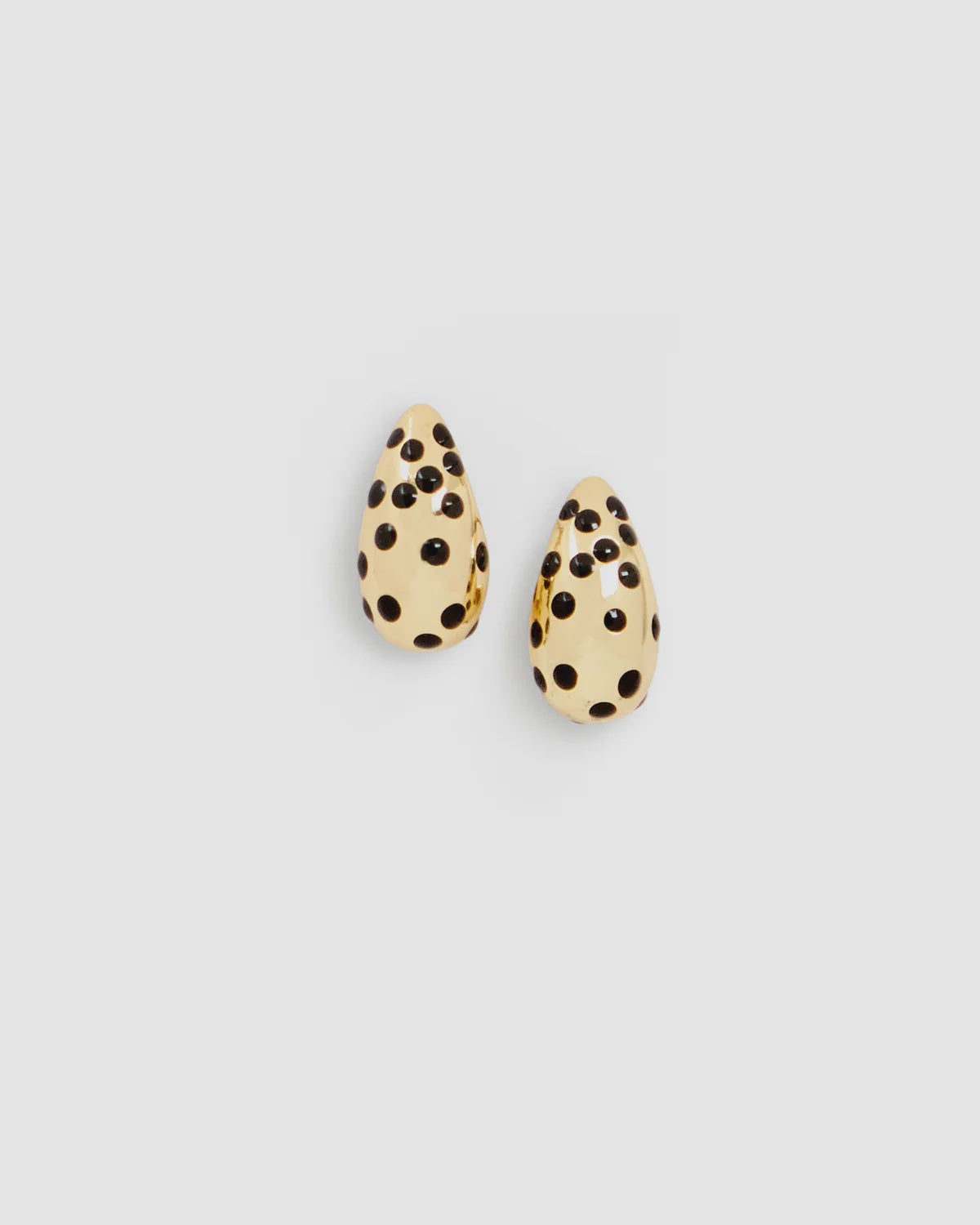 Gold-plated drop earrings with black polka dot enamel by Clare Vivier on a light gray background.