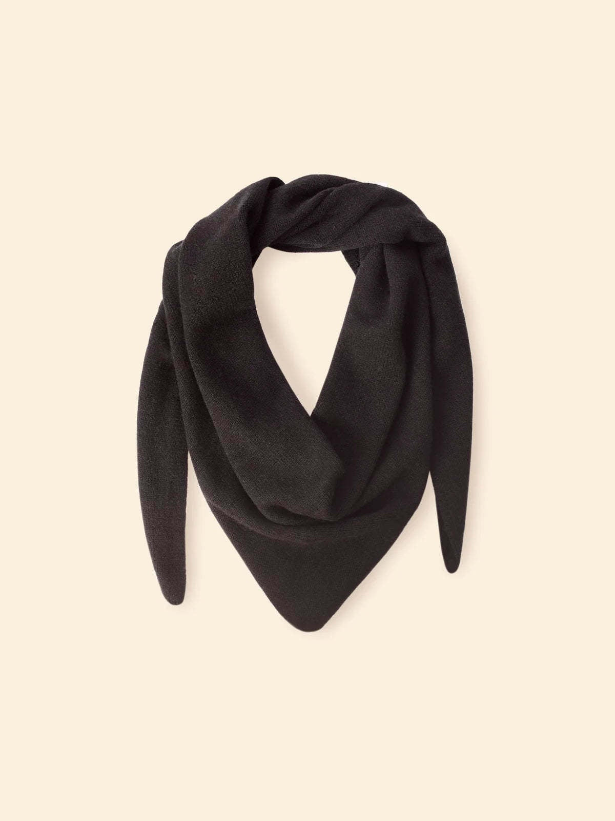 Le Petit Scarf, a black triangular cashmere piece with pointed ends, is made in Los Angeles and draped in a loose loop against a beige background.