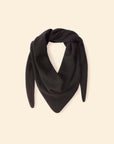 Le Petit Scarf, a black triangular cashmere piece with pointed ends, is made in Los Angeles and draped in a loose loop against a beige background.
