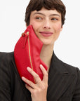 Clare Vivier Lips Flat Clutch in red held against a cheek, featuring a gold zipper.