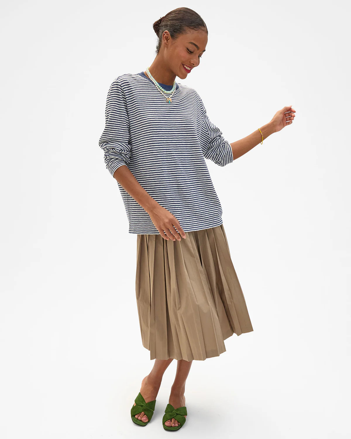 Tan pleated skirt and green sandals styled with a Clare Vivier long sleeve tee, minimal studio setting.