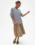 Tan pleated skirt and green sandals styled with a Clare Vivier long sleeve tee, minimal studio setting.