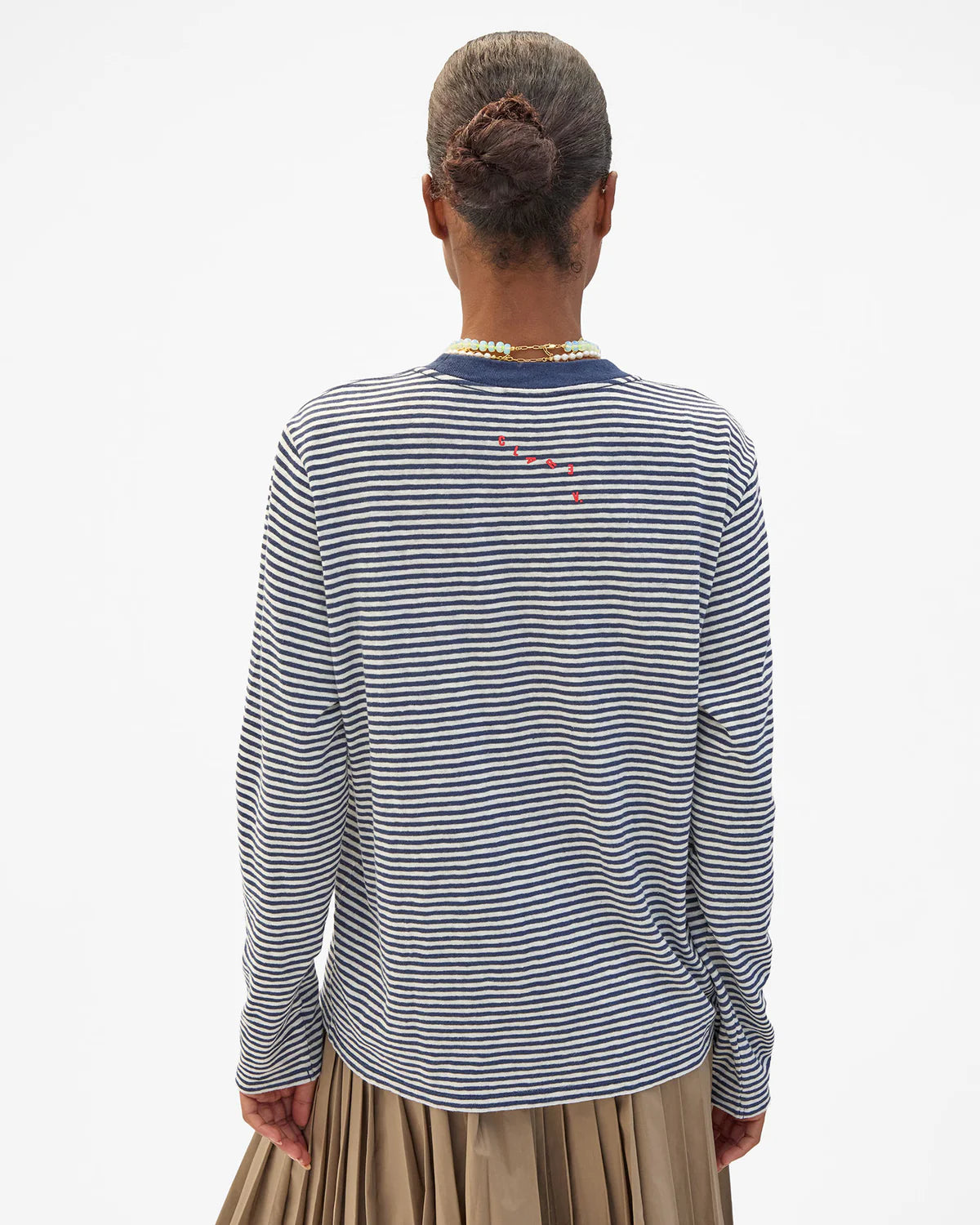 Blue and white striped Clare Vivier long sleeve tee with tan pleated skirt, seen from behind.