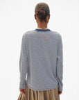Blue and white striped Clare Vivier long sleeve tee with tan pleated skirt, seen from behind.