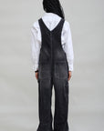 Black corduroy SLOUCH BIB OVERALL in a wide-leg cut, styled over a white long-sleeve shirt, back view.