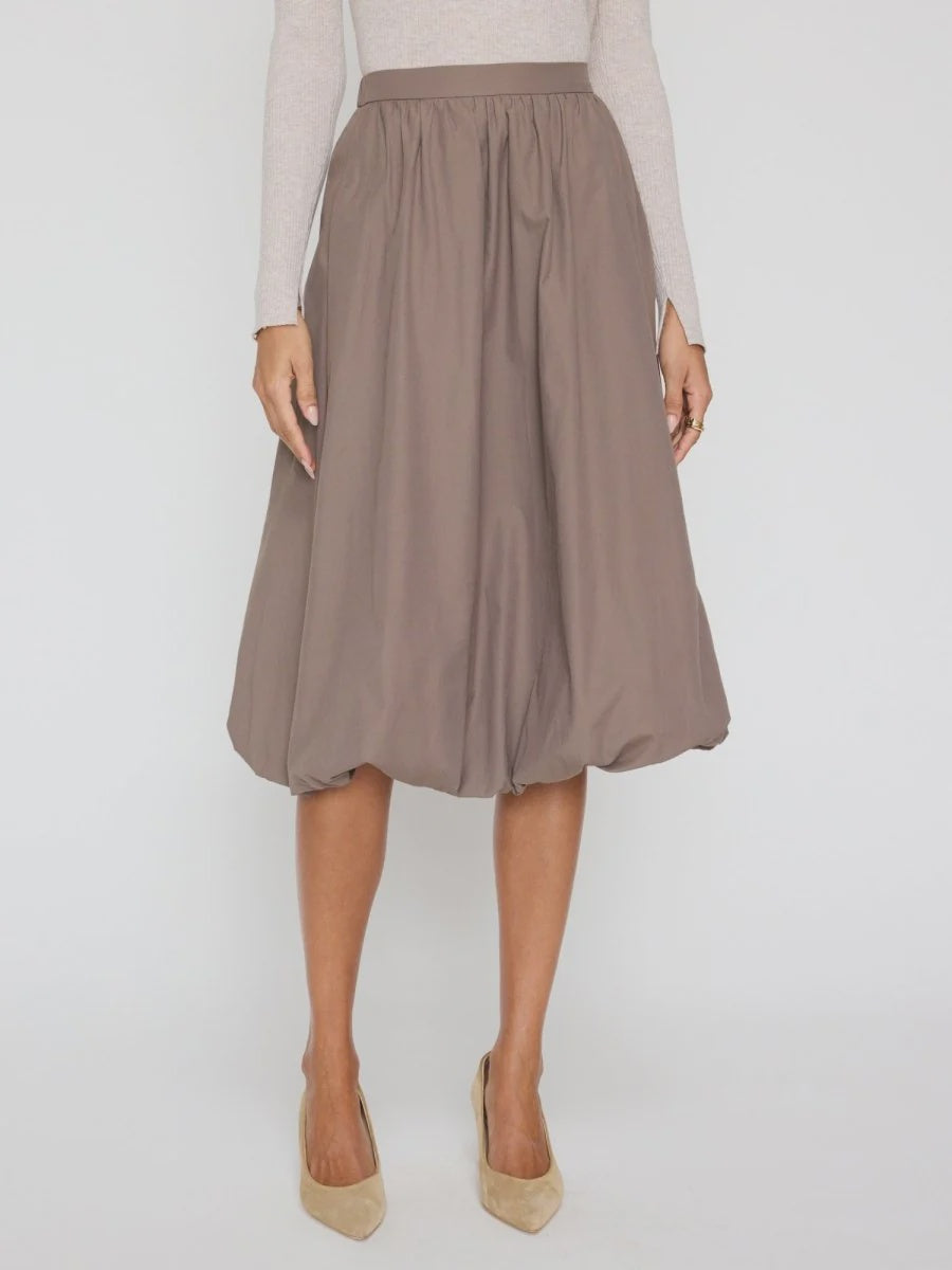 A person wears the BROCHU WALKER LOTI BUBBLE SKIRT in taupe—knee-length with a fitted waistband—paired with a light long-sleeve top and beige pointed-toe heels, standing against a plain background.