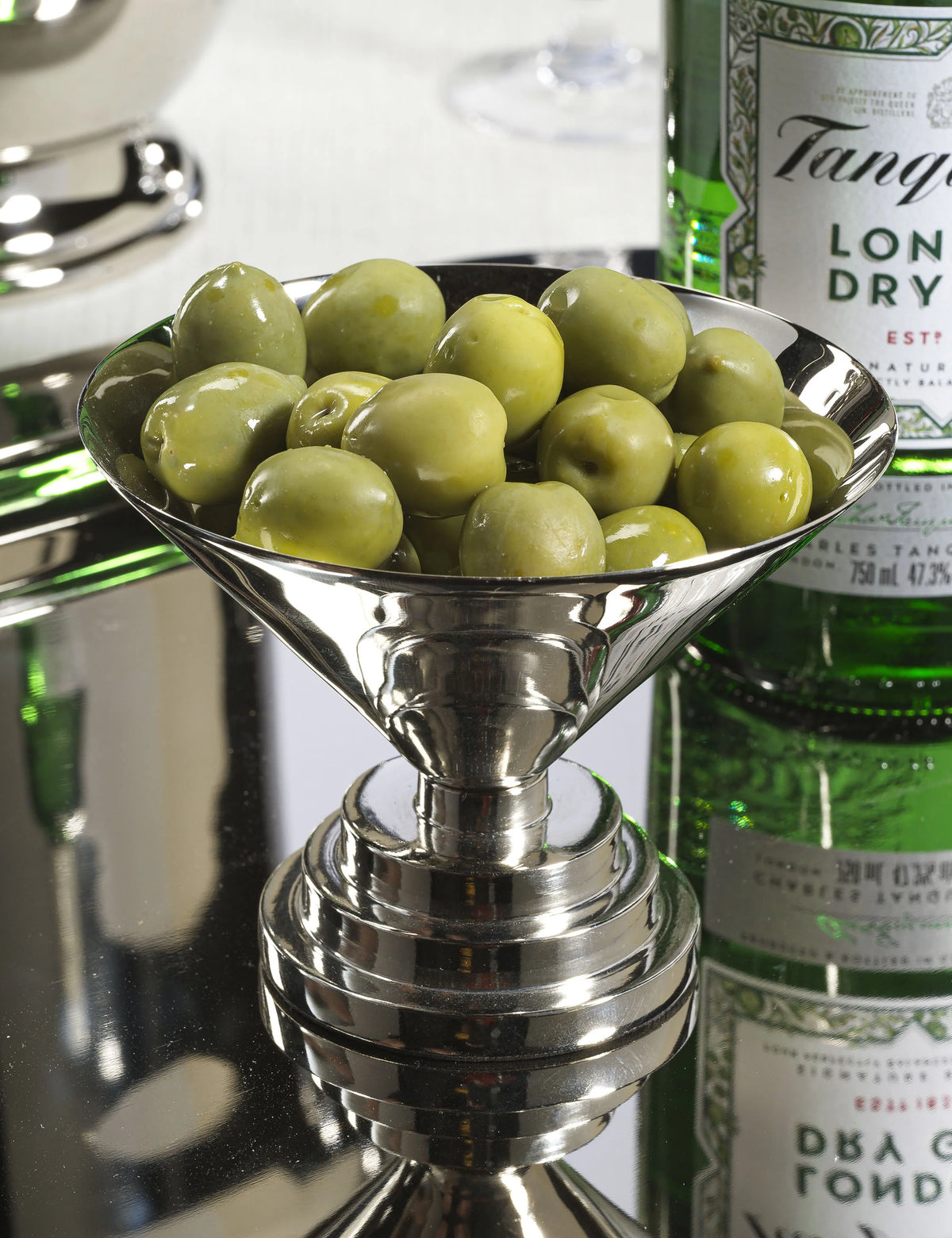 Nickel Zodax Condiment Bowl S filled with green olives on a reflective cocktail surface.