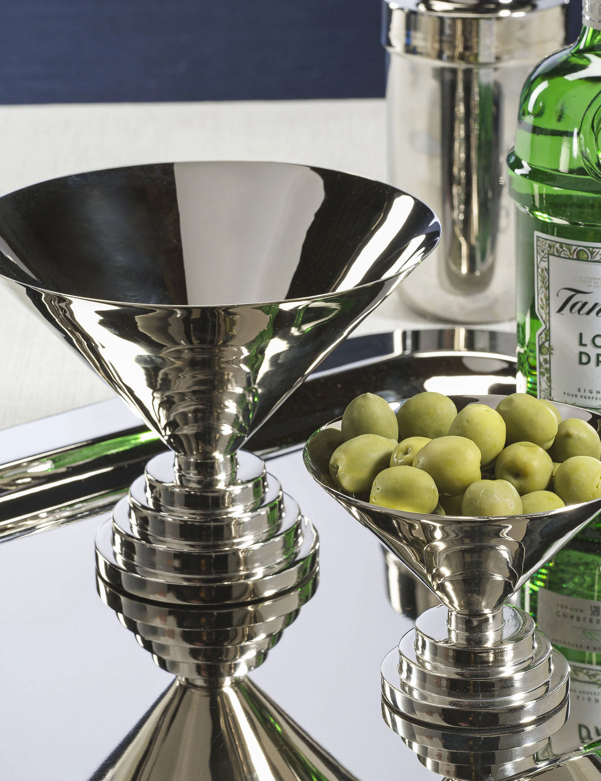 Nickel L Condiment Bowl with olives and matching stemmed bowl on a mirrored tray by Bungalow Furniture &amp; Accessories.