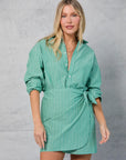 A woman with long blonde hair wears the Mamene Repeat Wrap Tennis Skirt, standing against a light gray textured background.