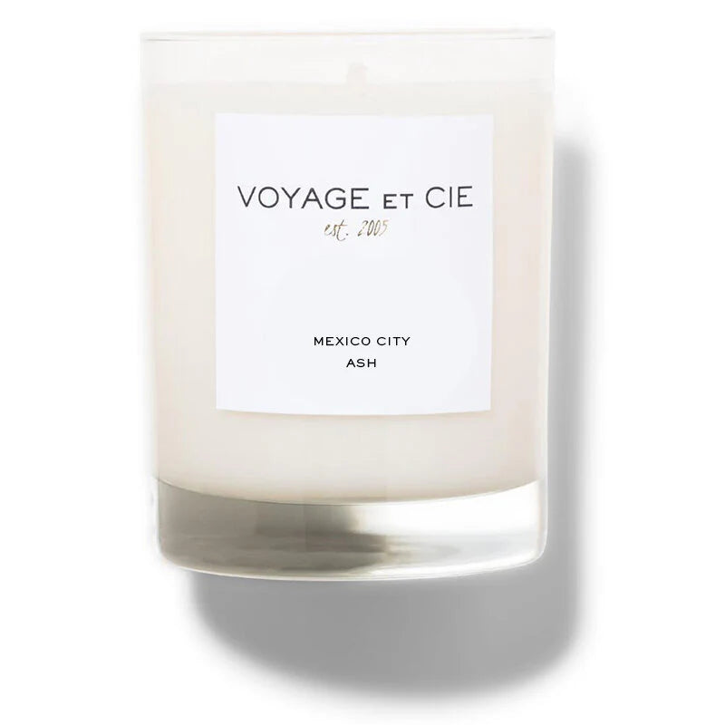 A white soy coconut blend candle from Voyage Et Cie, 14 OZ Classic Highball, sits in a clear glass jar labeled “VOYAGE ET CIE est. 2005, MEXICO CITY, ASH,” casting a soft shadow on a white background.