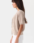Beige short-sleeved Mia Fratino Cashmere Rue Relaxed Cardigan with a button-front closure worn by a woman.