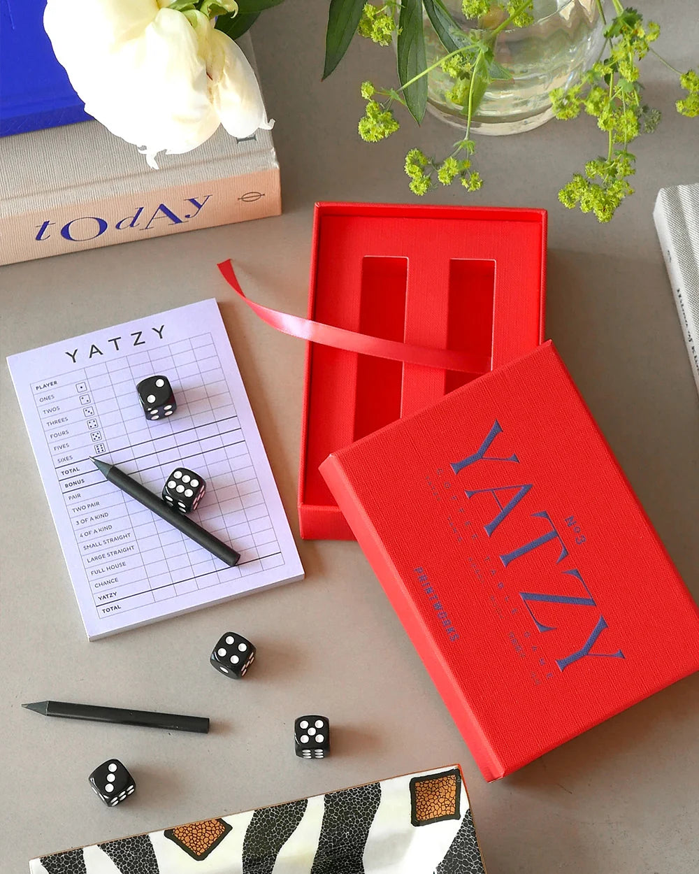 Printworks Yatzy game set in a red box with dice, pencils, and score pad on a table.