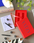Printworks Yatzy game set in a red box with dice, pencils, and score pad on a table.