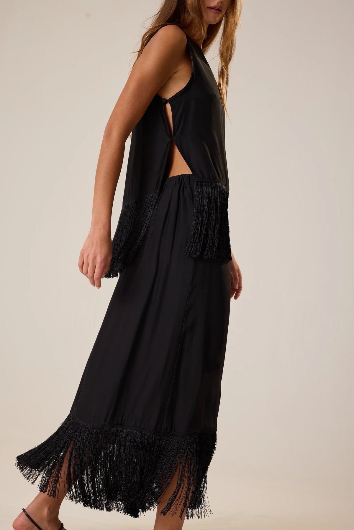 Sleeveless black Anita Skirt by Natalie Martin with fringe hem and side slit, shown in a modern lifestyle setting.