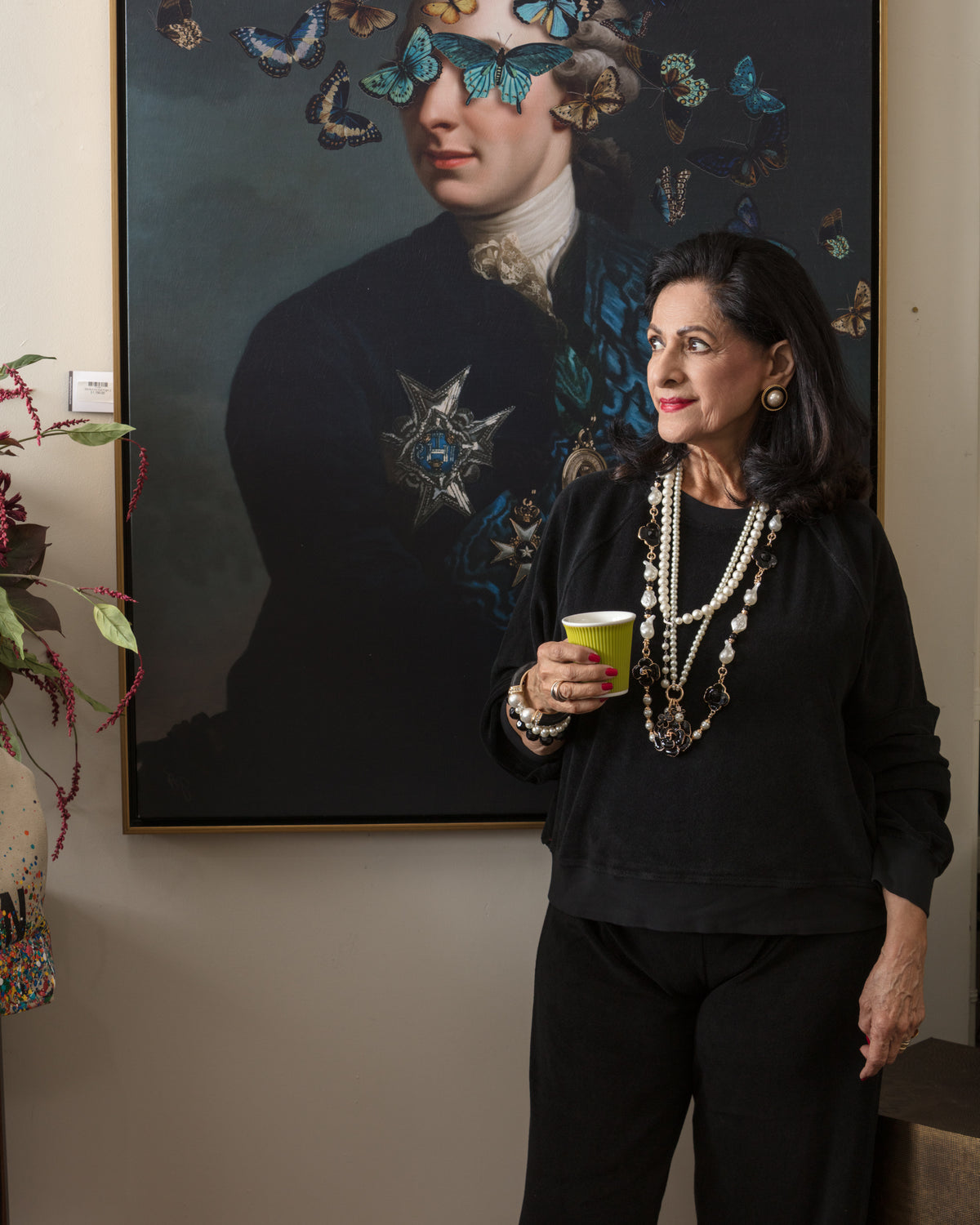 Yellow ceramic cup held by woman in black dress, styled before butterfly art at Bungalow Furniture & Accessories.