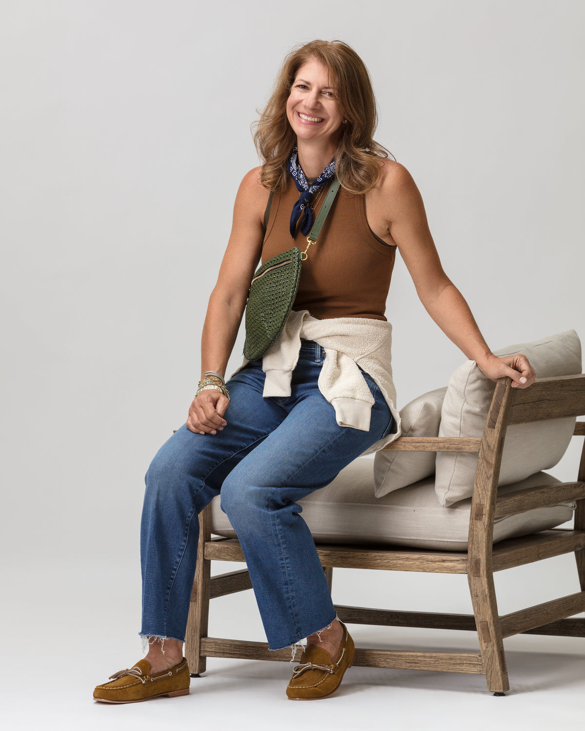 Woman in casual jeans and tank top sits on wood chair, showcasing relaxed Bungalow Furniture style.
