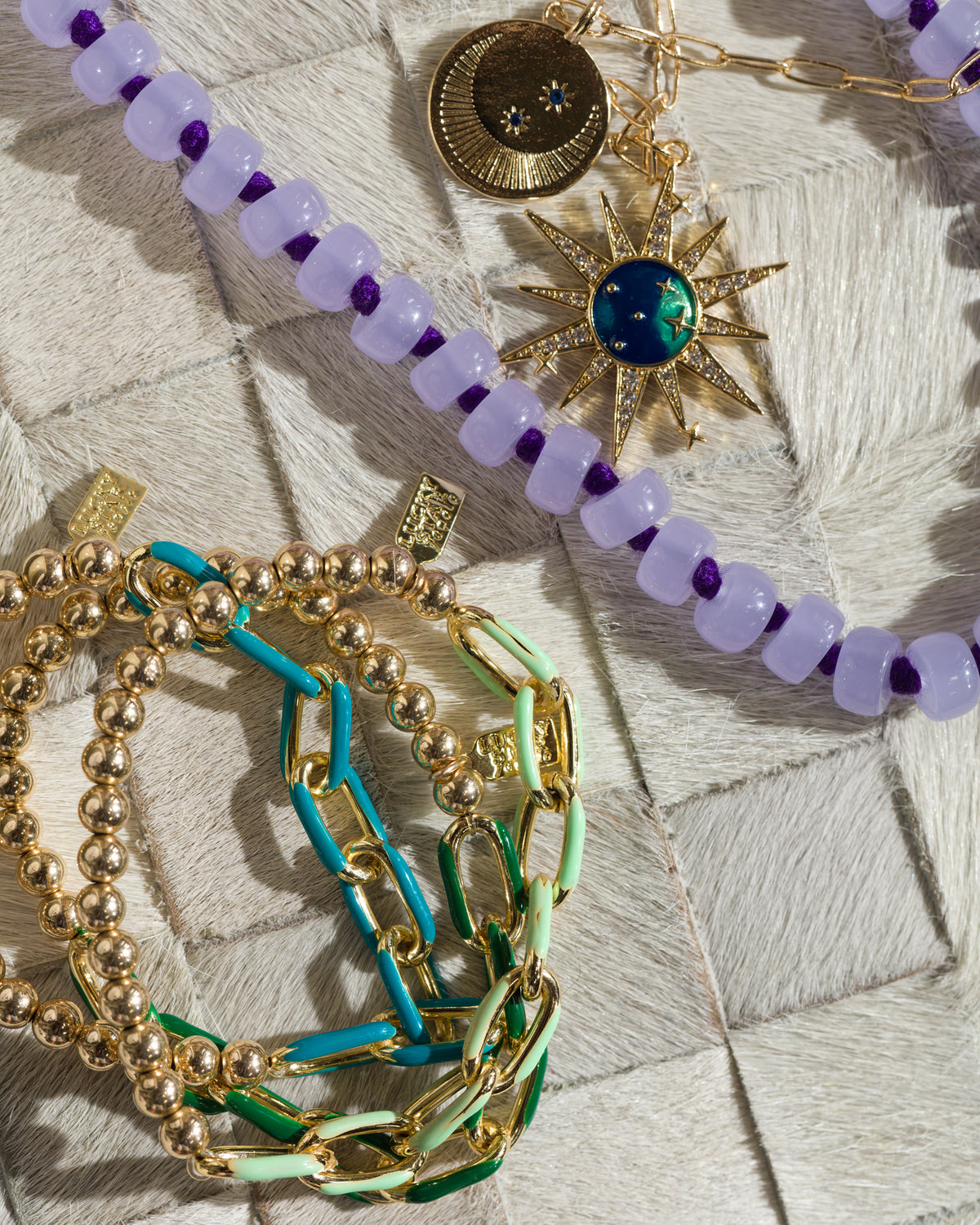 Gold and beaded bracelets with a purple necklace and gold star pendant on white, Bungalow Furniture & Accessories.