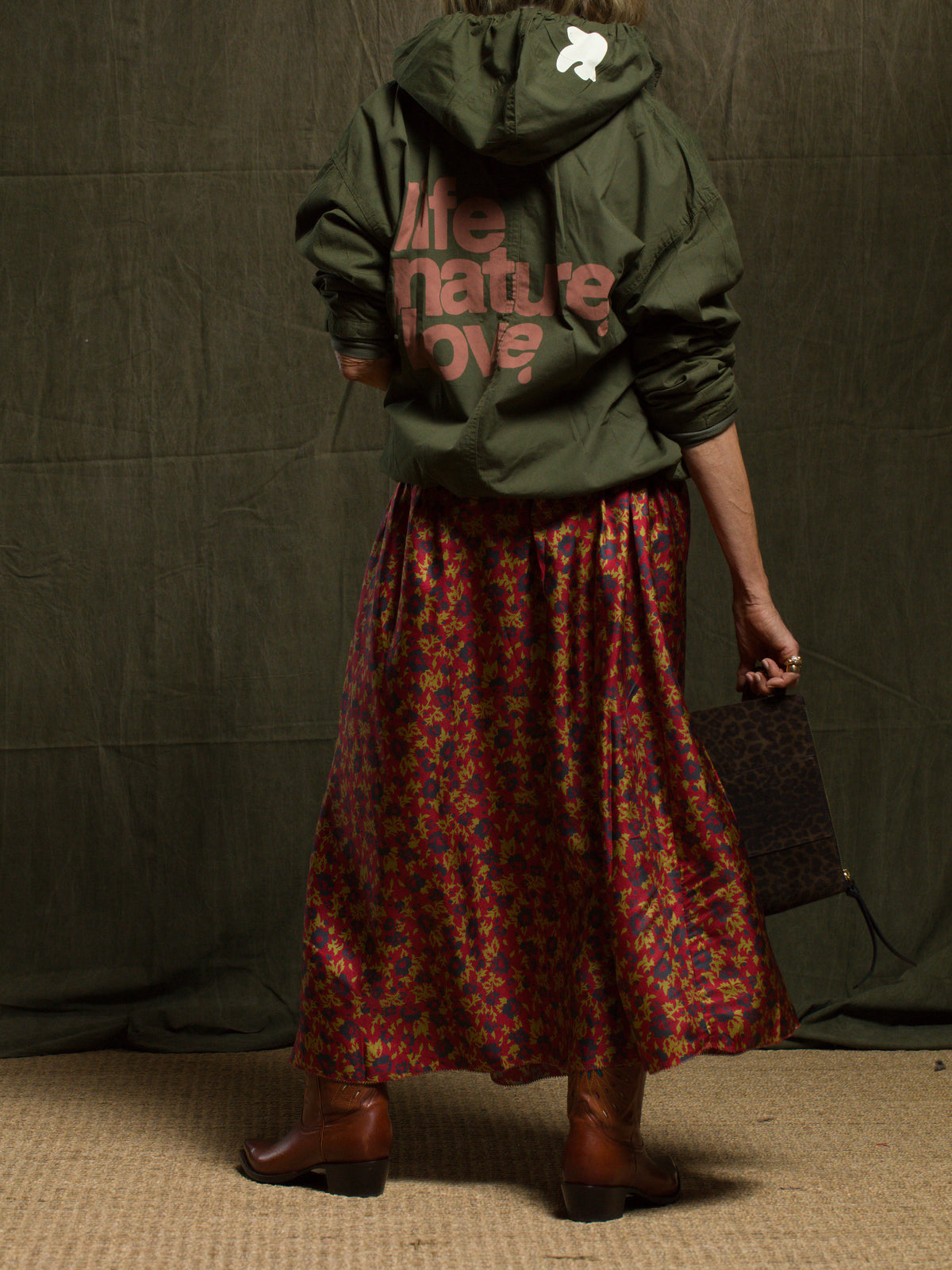 Free City LifeNatureLove RTU zip-up hoodie with floral skirt, brown boots, and dark clutch, shown from the back.