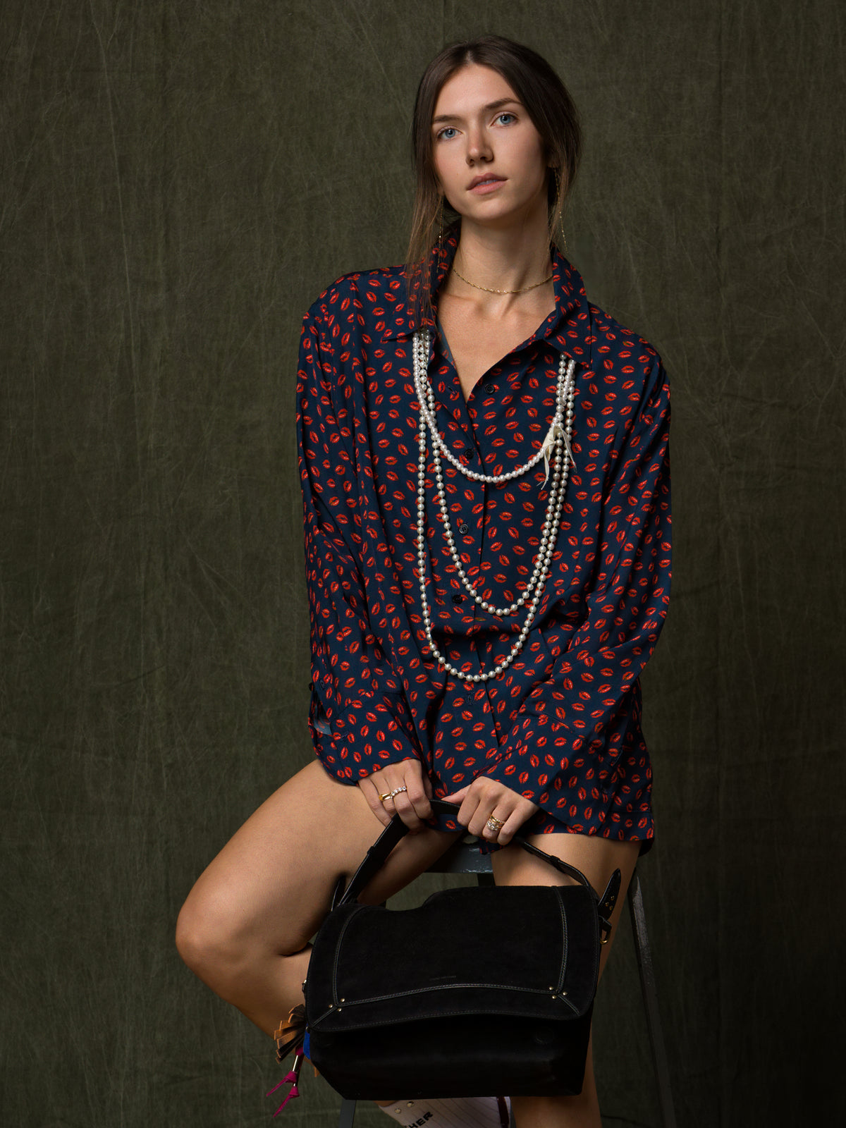 Black handbag held by woman wearing a patterned shirt and pearls, styled for Bungalow Furniture & Accessories.