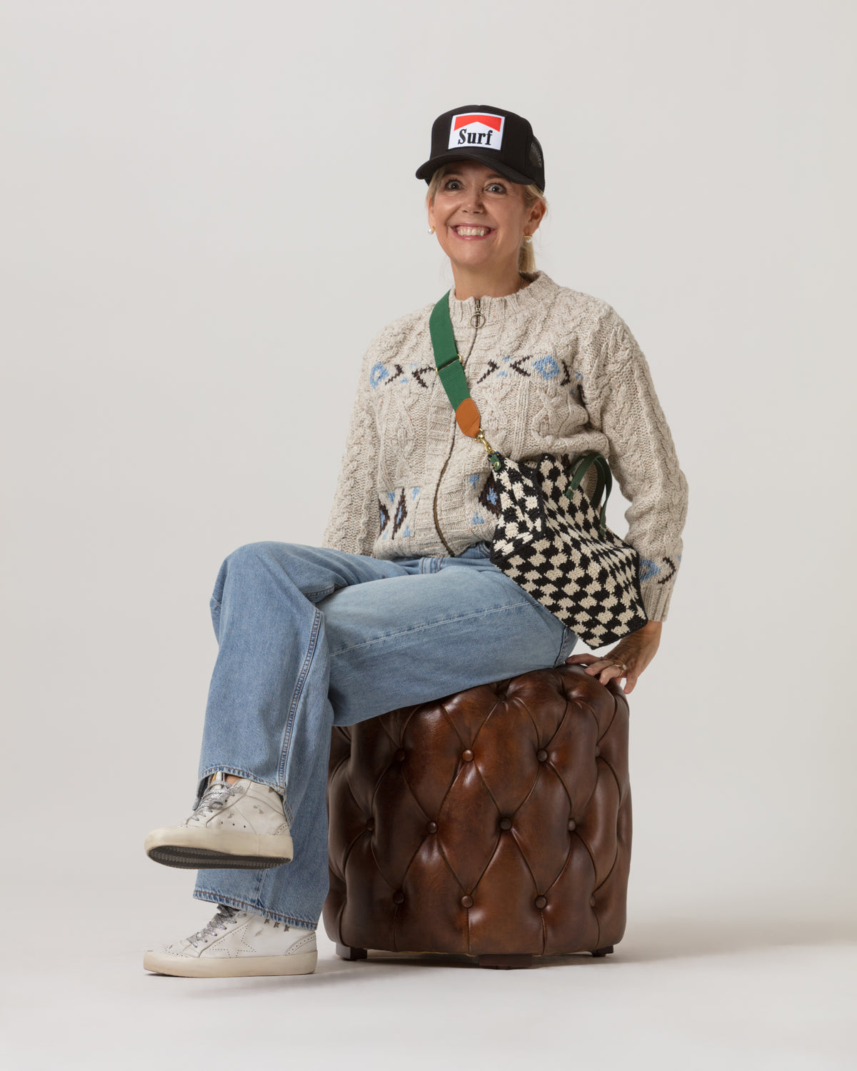 Brown ottoman with a checkered bag, styled in a cozy setting by Bungalow Furniture & Accessories.