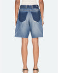 A person is seen from behind wearing Sea New York’s Milene Denim Knee Short—relaxed fit, high-waisted, vintage-inspired with large dark blue back pockets and frayed hems—styled with sandals and a sleeveless patterned top.