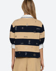 A woman with long, light brown hair wears the Sea New York Juliet SS Rugby—a loose, embroidered top with puff sleeves—layered over a white collared shirt. She faces away, showcasing this chic workwear-inspired style.