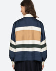A person with shoulder-length brown hair is seen from the back wearing the Sea New York Juliet Polo, a loose modern-fit jacket with wide navy, tan, white, and dark green stripes and voluminous sleeves, against a plain light background.