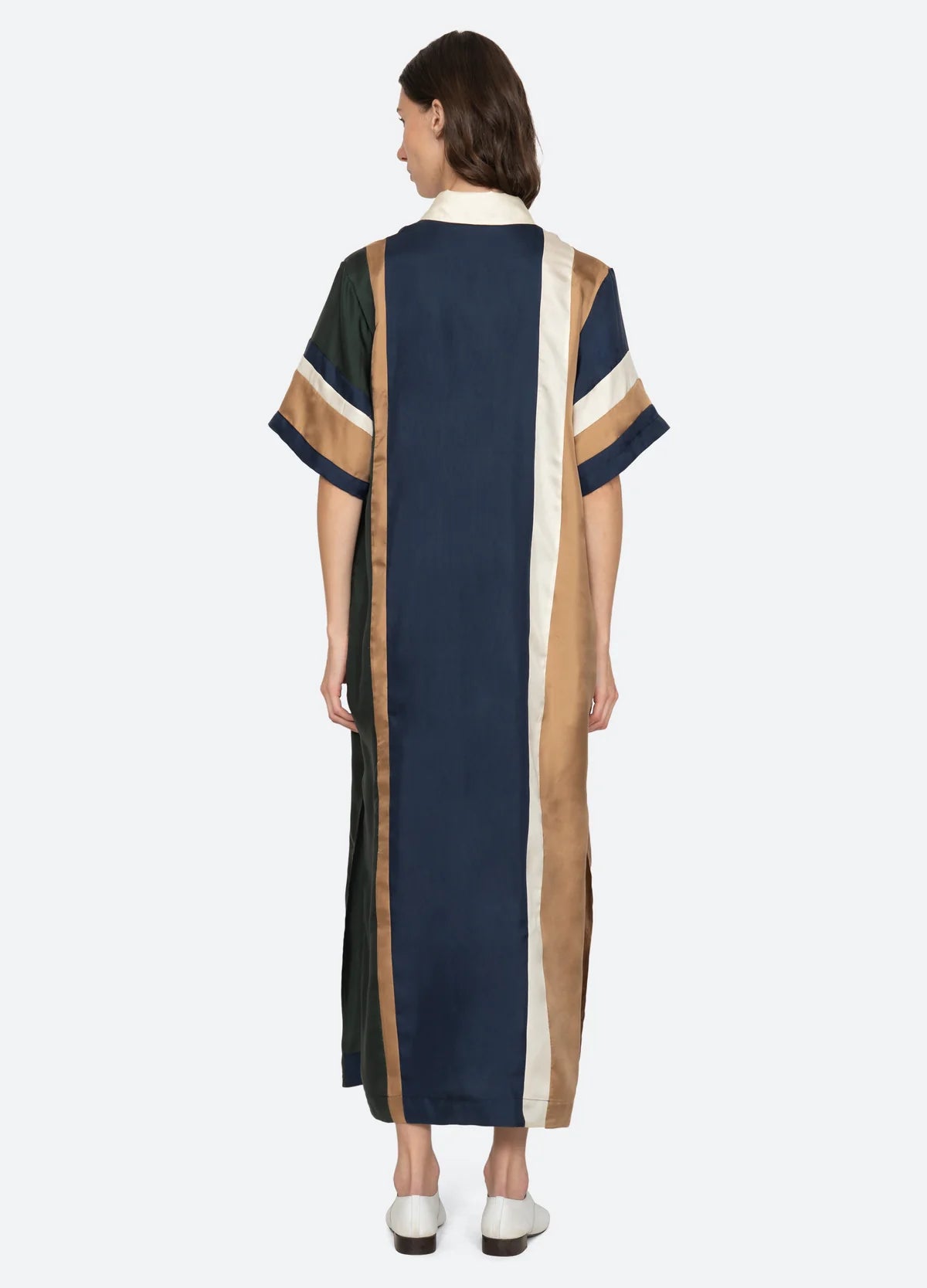 A person with short brown hair wears white shoes and the Sea New York Juliet Polo Maxi Dress—color-blocked with vertical navy, cream, and brown stripes and matching short sleeves—while facing away.