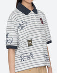 Wearing the Sea New York Winslow Craft Polo Shirt, this person sports a relaxed fit, short sleeves, striped design with embroidered animals, bird details, decorative patches, and dark collar and cuffs. Face is partially out of frame.
