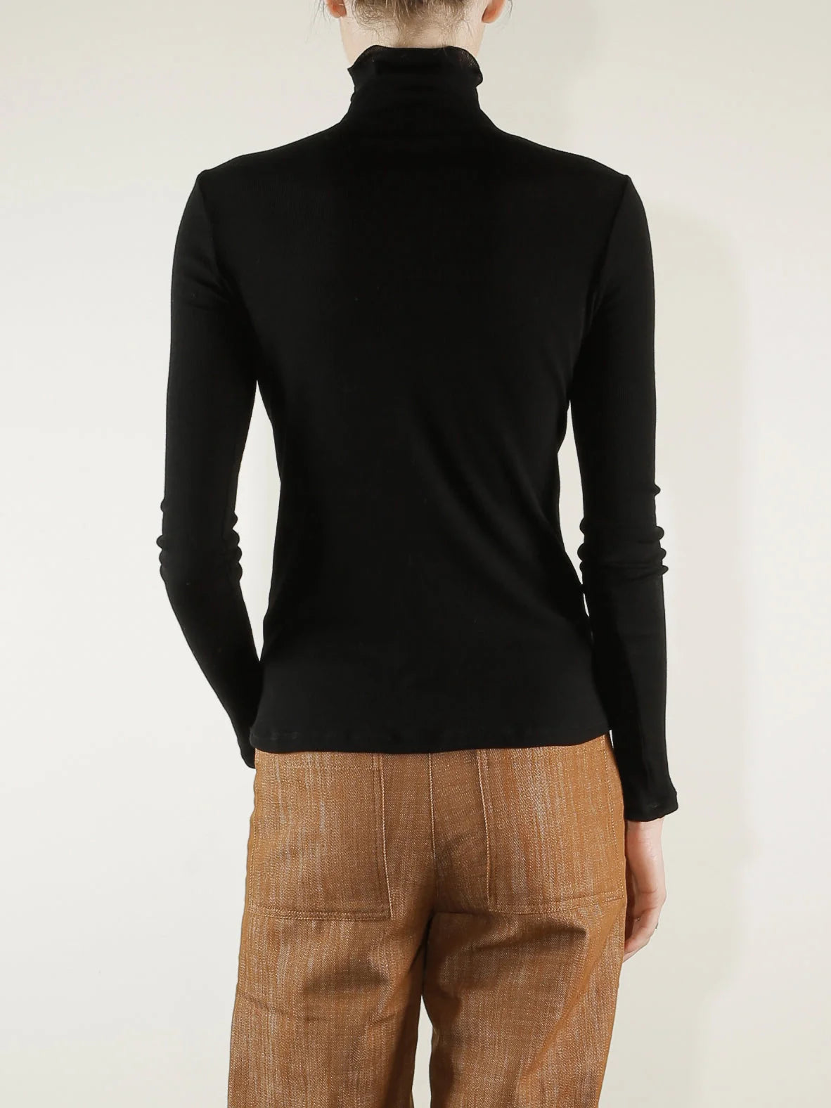 Black Pharaoh Cleo Turtleneck in lightweight rib, back view, styled with brown pants by Bungalow Furniture &amp; Accessories.