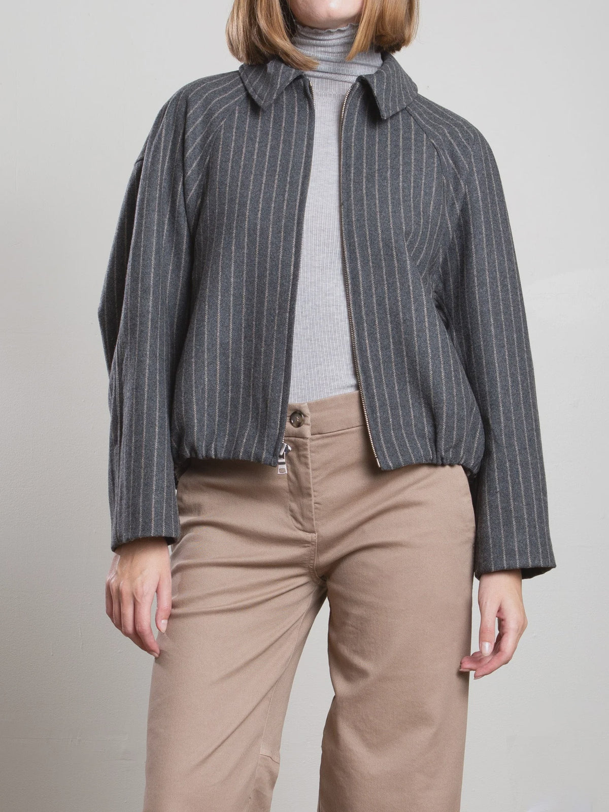 Pharaoh Andre Bomber Jacket in wool pinstripe, styled with a light gray turtleneck and beige pants.